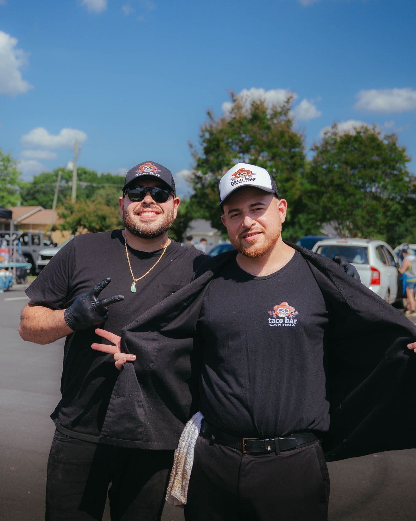 Two Taco Bar Cantina team members in branded caps, smiling outdoors at a catering event